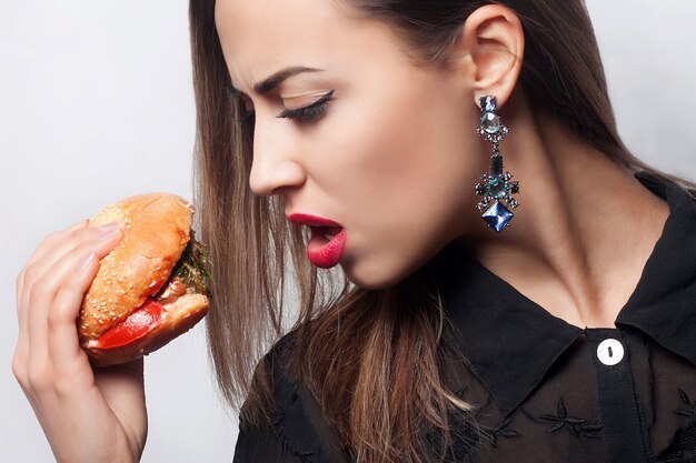 Close-up portret pięknej brunetki jedzącej dużego hamburgera