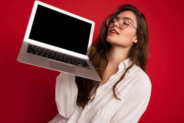 Close-up portret pięknej uśmiechniętej szczęśliwej młodej kobiety posiadania komputera przenośnego patrząc na netbook zabawy na sobie dorywczo inteligentne ubrania na białym tle