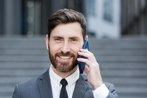 Close-up portretowe zdjęcie odnoszącego sukcesy brodatego biznesmena uśmiechniętego rozmawiającego przez telefon