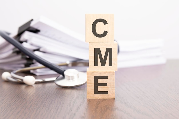 "CME Continuing Medical Education" jest napisane na drewnianym bloku w pobliżu stetoskopu na szarym tle