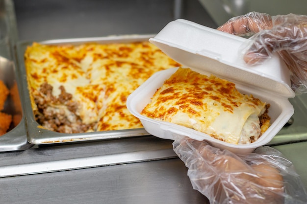 Cocinero toma pedazo de lasagna en un empaque de plastico para servir