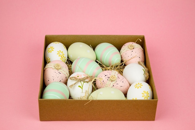 colorful easter eggs in cardboard box on pink background