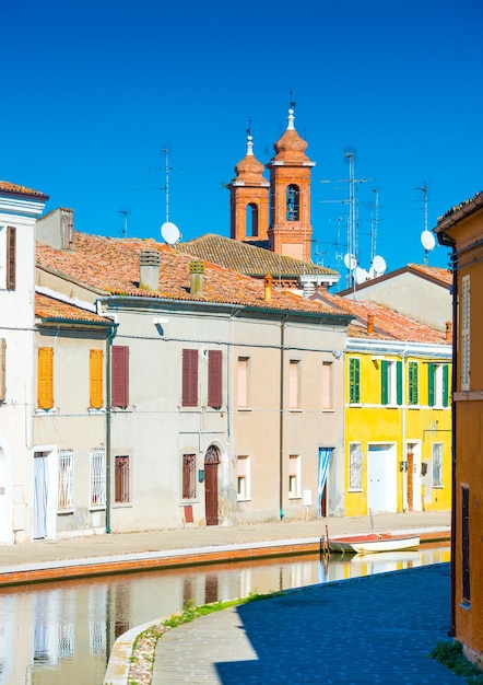 Comacchio, małe włoskie miasteczko znane również jako "Mała Wenecja", region Emilia Romagna, prowincja Ferrara, Włochy: Kolorowe domy w tradycyjnym stylu architektonicznym i kanał z łodzią w pobliżu