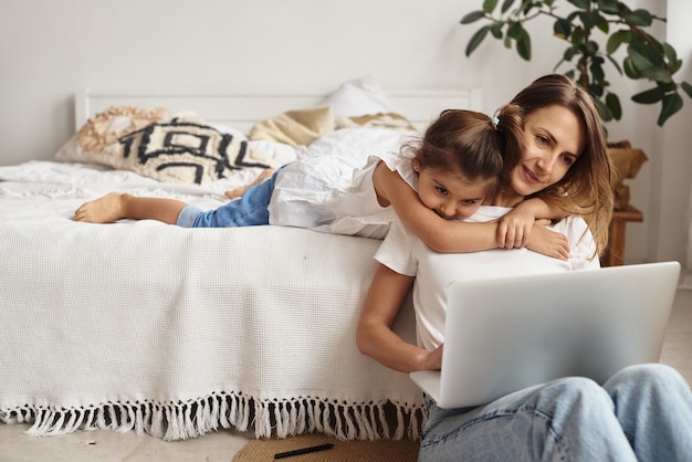 Córka bawi się z mamą i kotem, podczas gdy mama pracuje na komputerze