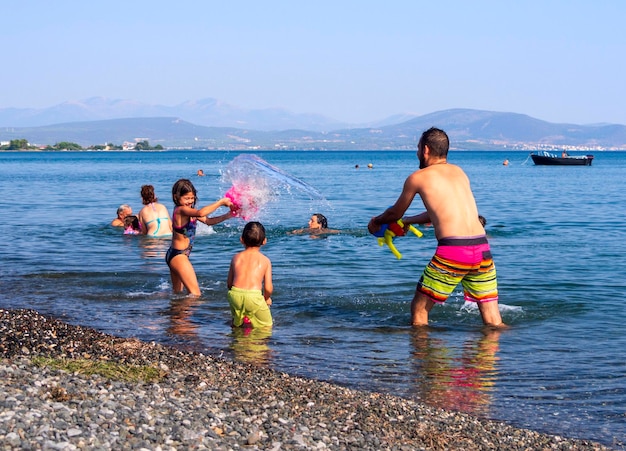 Córka i syn ojca rodzinnego bawią się i wylewają wodę na plaży na greckiej wyspie w letni dzień