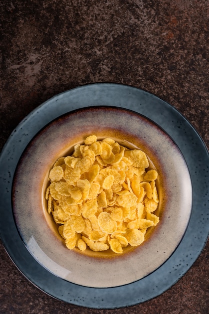 Cornflakes w ceramicznym talerzu na ciemnym tle. Śniadanie.
