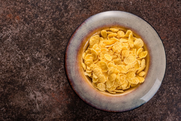 Cornflakes w ceramicznym talerzu na ciemnym tle. Śniadanie.