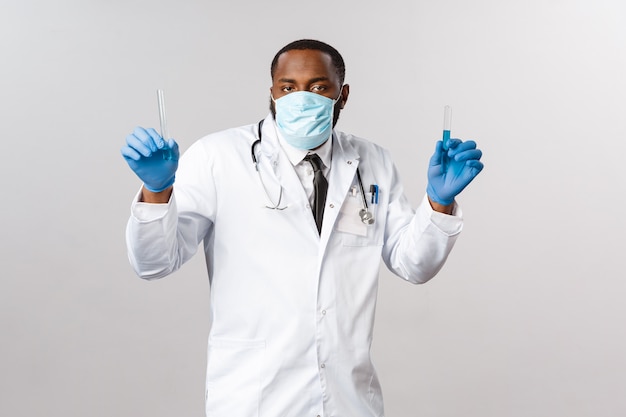 Covid-19, leczenie pacjenta koronawirusem i koncepcja laboratoryjna. Zabawny młody lekarz afroamerykański, naukowiec w lateksowych rękawiczkach i medycznej masce na twarz, trzymając probówki, fiolkę ze szczepionką i taniec