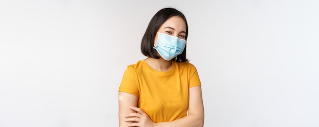 Covid szczepienia i koncepcja opieki zdrowotnej ładna azjatycka dziewczyna w medycznej masce na twarz trzymająca ramię z