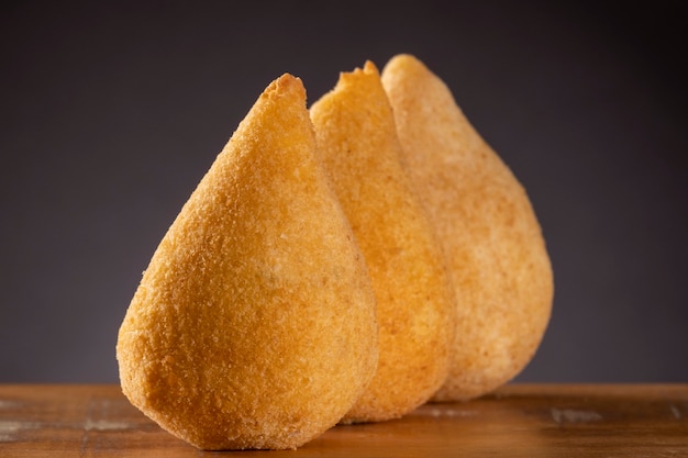 Coxinha smażona na drewnianym stole z brązowym tłem gradientowym.