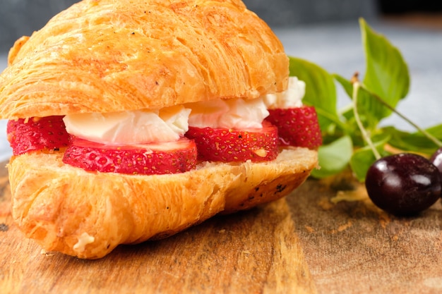 Zdjęcie croissant słodka kanapka z kremowym serem i truskawkami na drewnianej desce. przydatne śniadanie. odpowiednie odżywianie. tradycyjne francuskie potrawy.