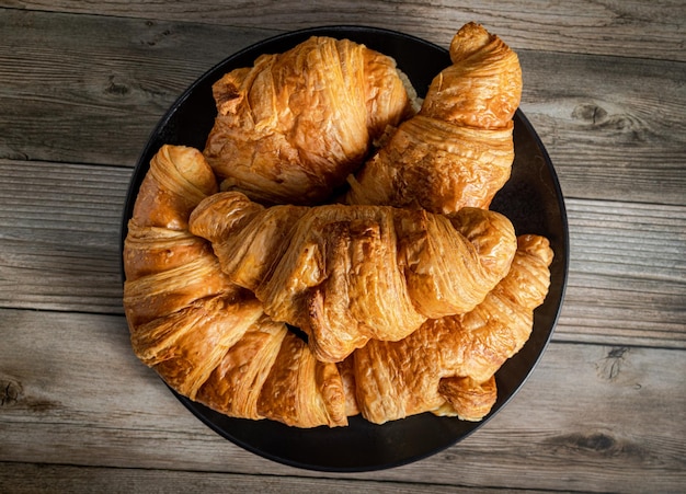 croissant sobre platon negreo sobre una mesa de madera pan frances croissant