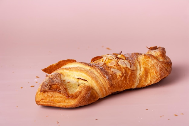 Croissant z marcepanem posypany migdałami na różowym tle zbliżenia