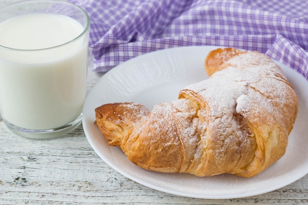 Croissant z mlekiem na starym drewnianym stole dla śniadaniowego tła.