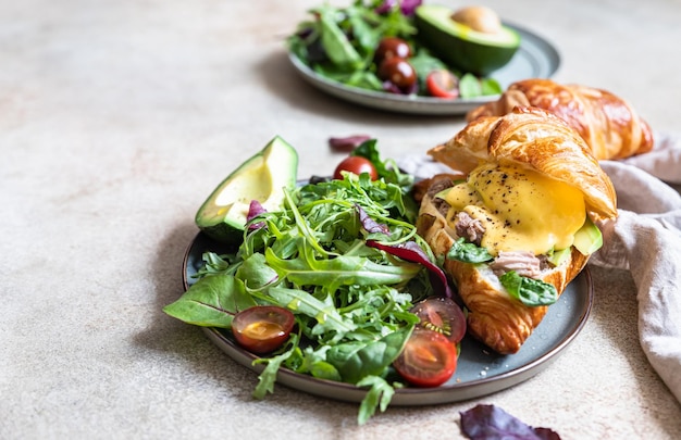 Zdjęcie croissant z tuńczykiem z jajkiem w koszulce awokado i sosem holenderskim z listkami sałat i pomidorami