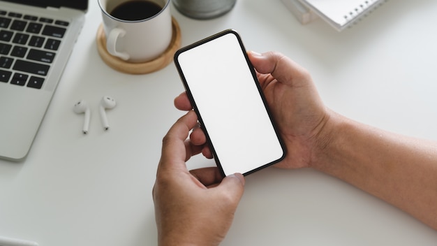 Cropped strzał biznesmena mienia telefon w workspace z innymi biurowymi dostawami na bielu stole