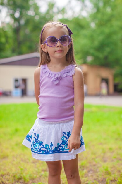 Cudowna mała dziewczynka chodzi przy lato parkiem w okularach przeciwsłonecznych