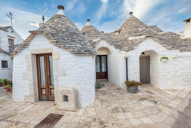 Cudowne miasto Alberobello z domami Trulli wśród zielonych roślin i kwiatów, główna dzielnica turystyczna, region Apulia, południowe Włochy. Typowe budynki zbudowane z suchego kamienia i stożkowego dachu