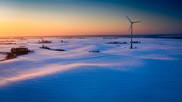 Cudowne ośnieżone pole i turbina wiatrowa o wschodzie słońca w zimie