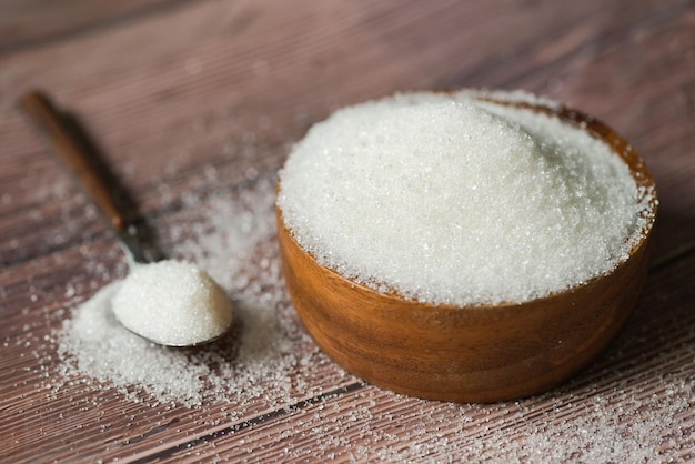Cukier na łyżce i drewnianej misce cukier biały do żywności i słodyczy kupa cukierków deserowych ze słodkiego cukru krystalicznego granulowanego