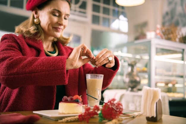 Cukier w latte. Stylowa, elegancka Francuzka, siedząc w piekarni, dodaje cukier do swojej latte