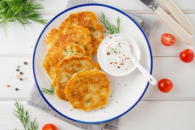 Zdjęcie cukierki ziemniaczane latkes lub draniki ze świeżymi ziołami i kwaśną śmietaną na talerzu