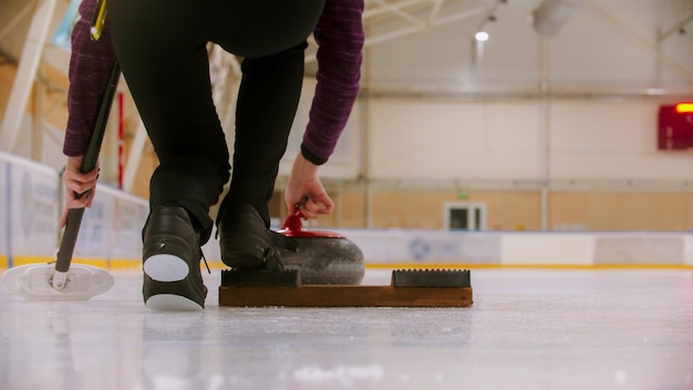 Curling Trenujący Kobietę, Która Ma Zamiar Zepchnąć Się Ze Stojaka Na Lodowisku