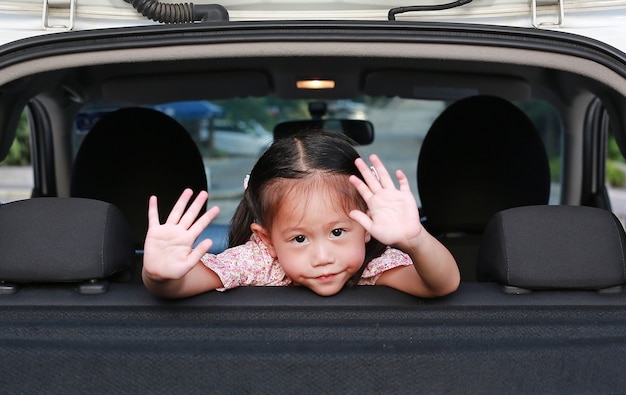 Cute asian girl na tylnym siedzeniu samochodu macha na pożegnanie.