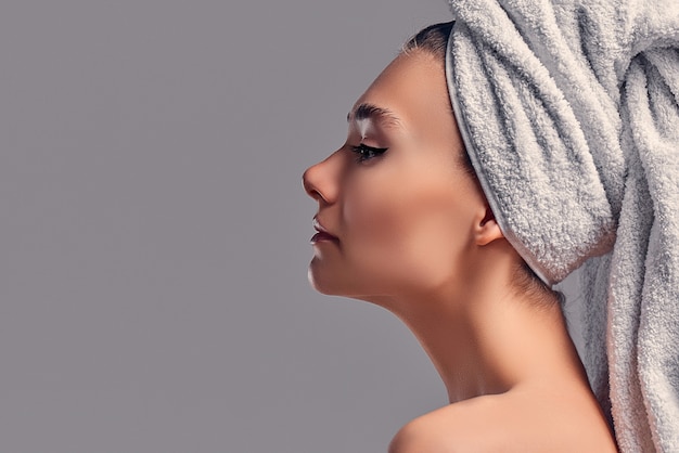 Cute atrakcyjna dziewczyna z ręcznikiem na głowie na białym tle na szarym tle. Koncepcja pielęgnacji skóry.