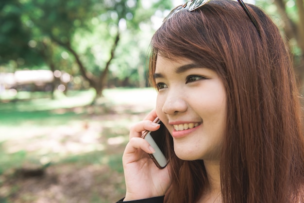 Cute azjatyckich kobieta mówi na telefon komórkowy, siedząc w parku w ciepłym dniu wiosennym.