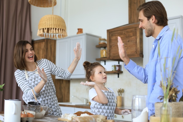 Zdjęcie cute dziewczynka i jej rodzice bawią się razem podczas gotowania w kuchni w domu.