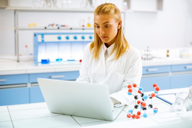 Cute kobieta naukowiec w białym fartuchu za pomocą laptopa podczas pracy w laboratorium