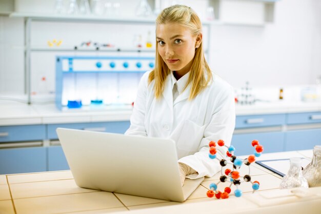 Cute kobieta naukowiec w białym fartuchu za pomocą laptopa podczas pracy w laboratorium