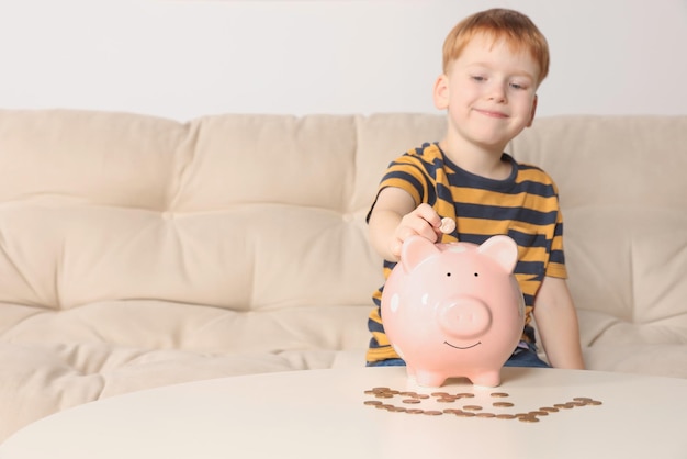 Cute little boy oddanie monety do skarbonki przy stole w pomieszczeniach skupić się na strony Przestrzeń dla tekstu