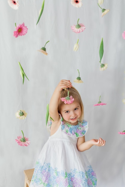 Cute little girl 3 lata z blond włosami z kolorowymi kwiatami na białym tle Święta wiosny Szczęśliwe dziecko