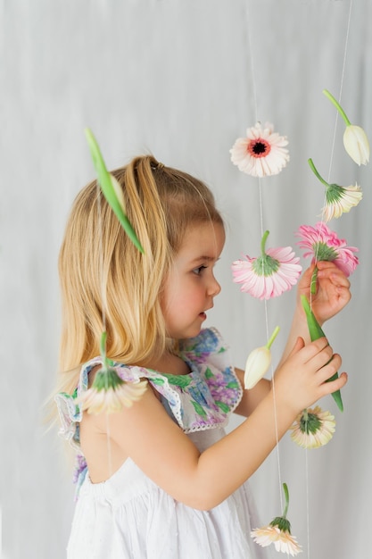 Cute little girl 3 lata z blond włosami z kolorowymi kwiatami na białym tle Święta wiosny Szczęśliwe dziecko