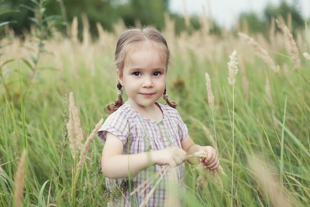 Cute little girl idzie przez pole pszenicy, uśmiecha się i patrzy w kamerę.