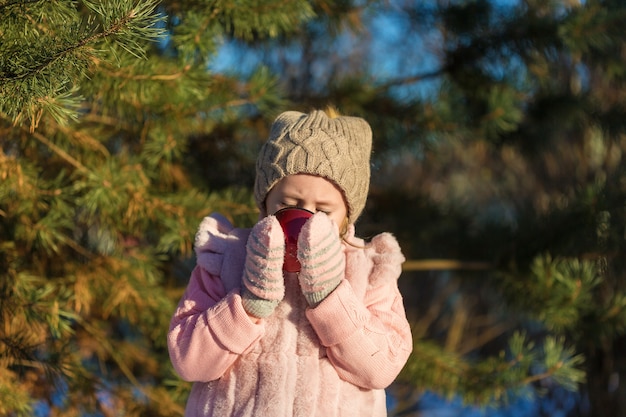 Cute Little girl pije z filiżanki w zimowym lesie. Szczęśliwe dzieciństwo. Koncepcja wakacje zabawy na świeżym powietrzu dla dzieci