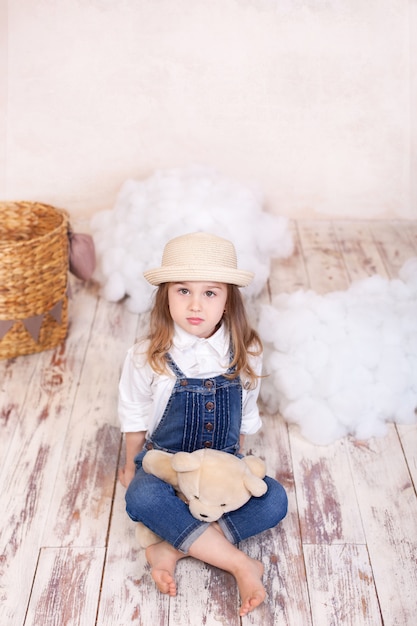 Cute Little Girl Siedzi Na Podłodze I Przytrzymaj Misia. Dziewczynka Bawi Się W Pokoju Dziecięcym Zabawką.