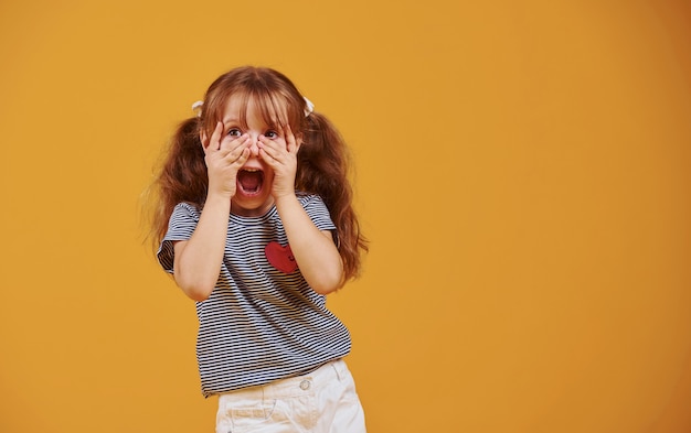 Cute little girl w ubranie bawić się w studio na żółtym tle.