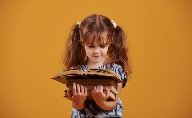 Cute little girl z książką w ręce w studio na żółtym tle.