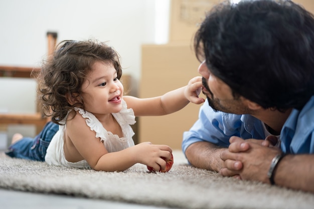 Cute little girl za pomocą palca dotknąć ust jej ojca, leżąc na podłodze w salonie