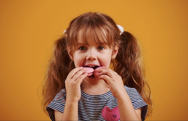Cute little girl ze słodkim jedzeniem w studio na żółtym tle.