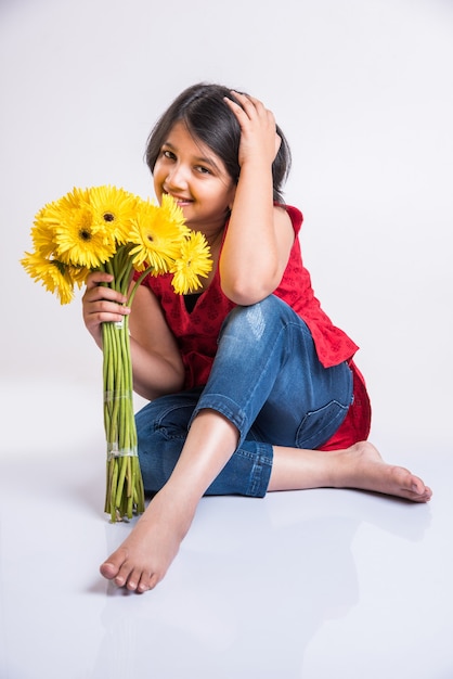 Cute Little Indian Girl trzyma kilka lub bukiet świeżych żółtych kwiatów Gerbera. Pojedynczo na białym tle