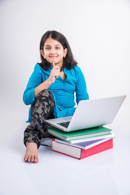 Cute little indyjskich lub azjatyckich dziewczyna dziecko studiuje na laptopie lub pracuje nad projektem szkolnym, leżąc lub siedząc na podłodze, na białym tle nad białym