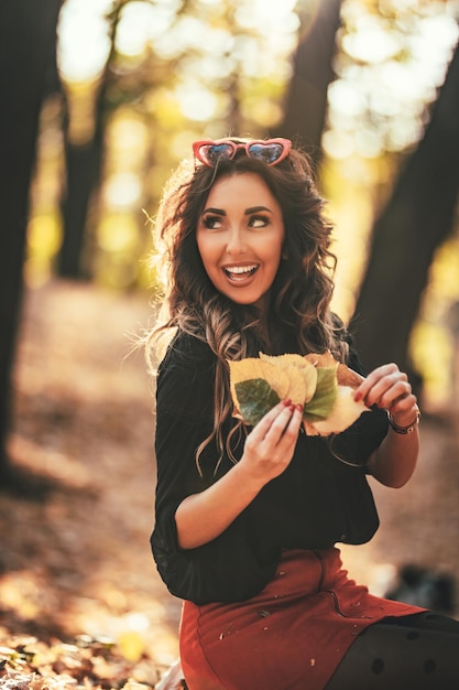 Cute młoda kobieta korzystających w słonecznym lesie w jesiennych kolorach. Ona trzyma złote żółte liście.