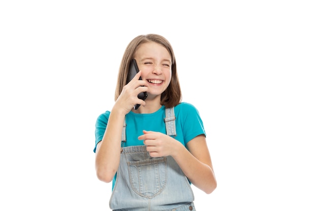 Cute teen dziewczyna w denim kombinezon rozmawia przez telefon i śmiejąc się. Pojedynczo na białym tle.