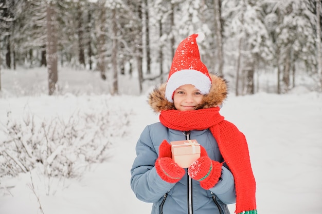 Cute teen girl otwiera pudełko prezent gwiazdkowy odkryty w zimie dziecko w rękawiczkach szalik i kapelusz santa