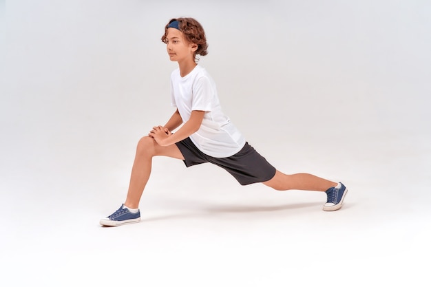 Ćwiczenia rozciągające na całej długości kaukaskiego wysportowanego nastoletniego chłopca w stroju sportowym przed rozgrzewką
