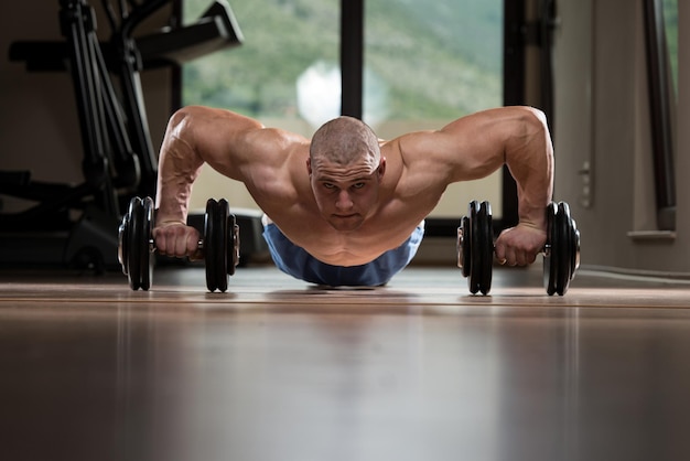 Zdjęcie Ćwiczenie siłowe pushup młodego mężczyzny z hantlami podczas treningu na siłowni